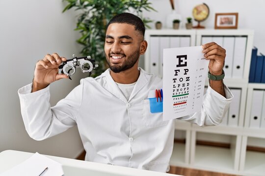 Young arab man holding sneller test and optometry glasses at clinic