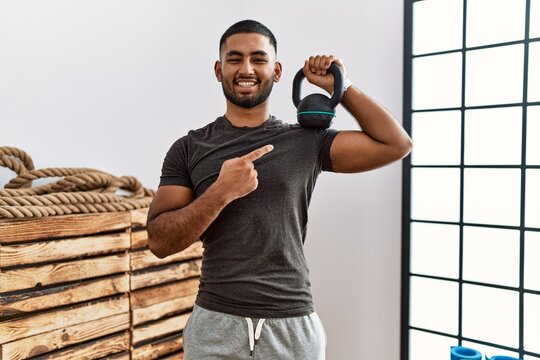 Young indian man wearing sportswear using dumbbells smiling happy pointing with hand and finger