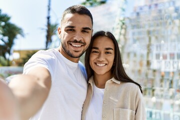 Fototapeta premium Young latin couple smiling happy and hugging making selfie by the camera at the city.