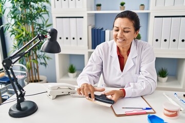 Obraz premium Middle age hispanic woman dentist holding whitening teeth test at clinic