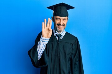 Middle age hispanic man wearing graduation cap and ceremony robe showing and pointing up with fingers number four while smiling confident and happy.