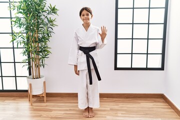 Young hispanic girl wearing karate kimono and black belt showing and pointing up with fingers number five while smiling confident and happy.