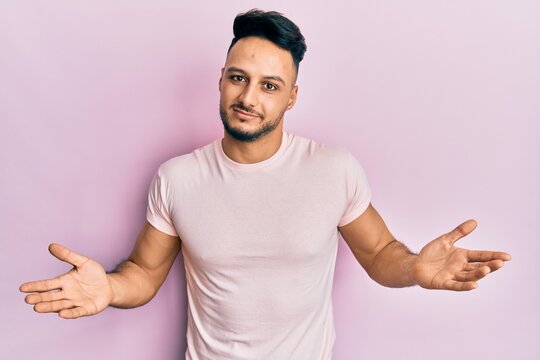 Young arab man wearing casual clothes clueless and confused expression with arms and hands raised. doubt concept.