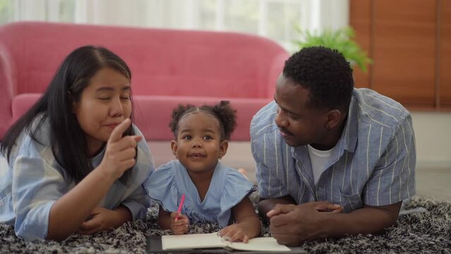 Portrait happy love african family father and mother with little asian girl learn and study on table.Mom and dad with asian girl writing with book make homework in homeschool at home.Education	