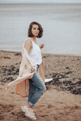 A girl in a pale pink raincoat and a white T-shirt walks alone along the sandy beach
