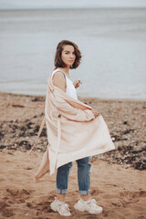 A girl in a pale pink raincoat and a white T-shirt walks alone along the sandy beach