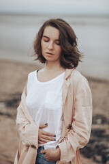 A girl in a pale pink raincoat and a white T-shirt walks alone along the sandy beach