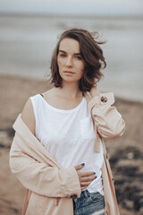 A girl in a pale pink raincoat and a white T-shirt walks alone along the sandy beach