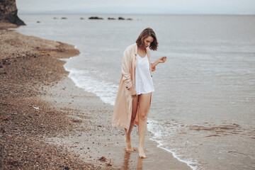 A girl in a pale pink raincoat and a white T-shirt walks alone along the sandy beach