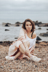 Fototapeta na wymiar A girl in a pale pink raincoat and a white T-shirt walks alone along the sandy beach