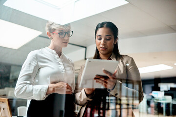 Utilising apps thatll help them come out on top. Shot of two businesswomen using a digital tablet together in an office.