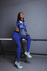 Naklejka premium athletic dark-haired girl in a blue tracksuit and blue sneakers sits on the edge of the table