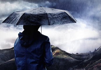 A storm is brewing. Shot of a woman covered with an umbrella watching a thunderstorm over a...