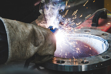 A welder is welding a flange assembly to a water pipe system.