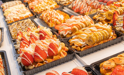 Delicious traditional Liege waffles with colorful toppings on display in a store window in Brussels, Belgium. Sugary desserts. Typical Belgian sweet food.