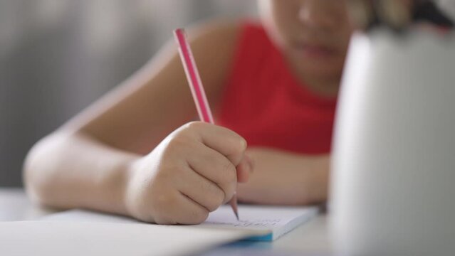 closeup hand of asian child write learning or kid girl student doing homework on book to learn from homeschool and person training writing on paper and desk by back to school to study online class