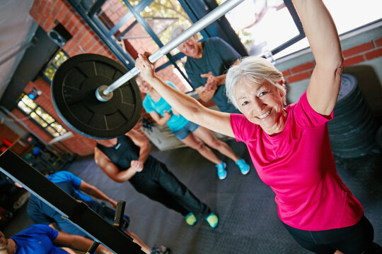 It doesnt get easier, you get stronger. Shot of a senior woman lifting weights while a group of people in the background watch on.