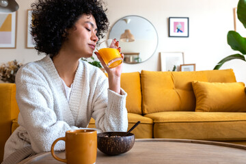 Relaxed African American woman drinks orange juice for breakfast at home. Copy space.