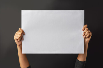 Leave your message here. Shot of a person holding up a blank page against a dark background.