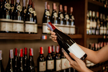 Women Hand Picking up Red Wine Bottle from Alcohol Shelf at Wine Store Shop.Vintage tone