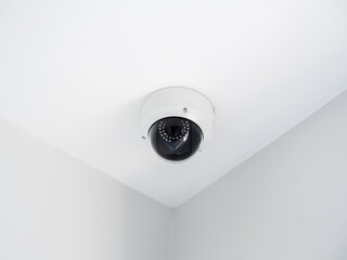 Digital security eye. A white round indoor CCTV surveillance camera monitoring security on ceiling...