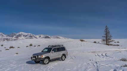 The SUV is parked on a snowy valley. Tire tracks and footprints in the snow around. A lonely...