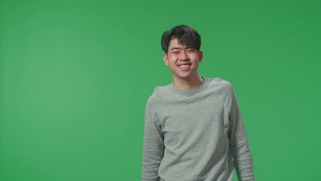 A Smiling Asian Man Dabbing While Standing In Front Of Green Screen Background  
