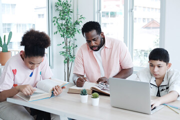 Obraz premium Young African teacher or tutor is reading a book and teaching for knowledge about online research with internet on laptop for Caucasian student boy in classroom. Education and Technology Concept.