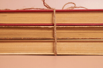 A stack of old battered books tied with a jute rope on a colored background