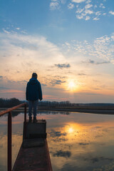 Naklejka na ściany i meble Small boy, child in jacket standing on water gate pond shore at sunset. Czech landscape
