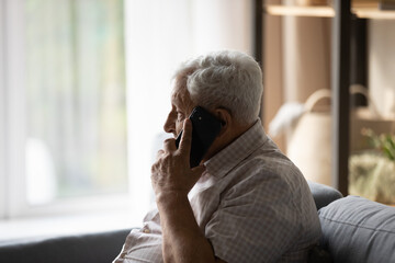 Elderly man holding smartphone talking sit on sofa in living room, having distant communication with doctor get services or recommendations from therapist. Older gen citizen using modern tech concept