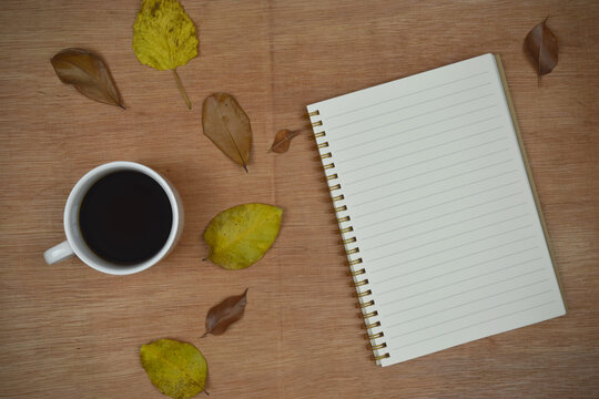 coffee and notebook with autumn leaves on wooden background. copy space.