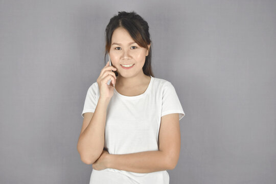 Beautiful young asian woman talking smart phone and smile standing on grey background.