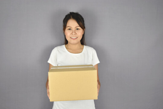 Asian woman smiling holding package box on grey background.