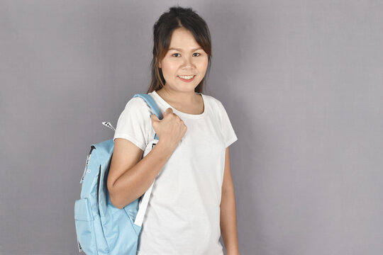 young woman with backpack standing and smiling on grey background.