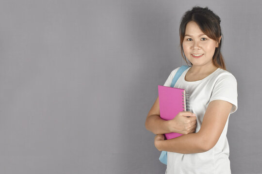young woman holding backpack and notebooks standing on grey background.