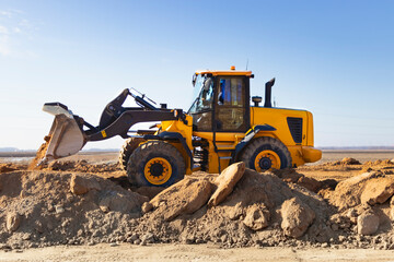 Bulldozer or loader moves the earth at the construction site against the blue sky. An earthmoving...
