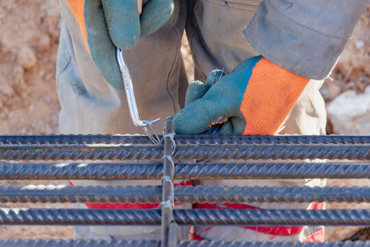 A worker uses steel tying wire to fasten steel rods to reinforcement bars. Close-up. Reinforced concrete structures - knitting of a metal reinforcing cage.