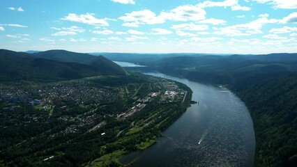 Flying drone along wide river and mountains, hydroelectric power plant in background. Height of bird's flight. Aerial view of beautiful drone shot of Divnogorsk city near Yenisei river.