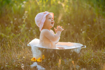 baby in a pink panama hat is sitting in an iron bubble bath in the garden and blowing soap bubbles