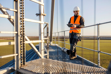 An industry worker standing on top of the silo and scrolling on tablet. © Dusan Petkovic