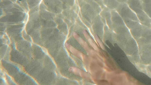 Amazingly beautiful abstract background with pattern of sun rays made by ocean ripples and male hand hitting the bottom creating a white sand cloud. Touching nature in tropical paradise. Sea bathing.