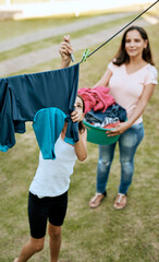 Learning to be responsible one peg at a time. Shot of a mother and daughter hanging up laundry together outside.
