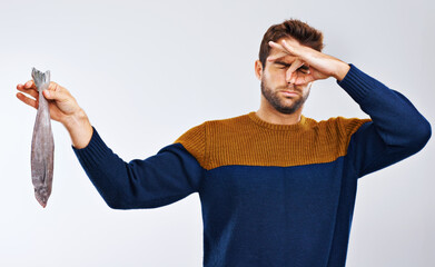 Stings the nostrils....yuck. Studio shot of a man showing disgust while holding a smelly fish.