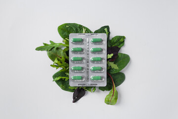 Silver blister with diet supplements in green capsules on the green leaves of arugula and lettuce. Health care concept. - obrazy, fototapety, plakaty