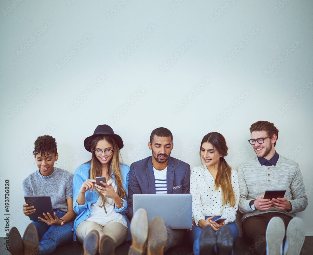 Poster Making the right connections as a team. Studio shot of a group of young businesspeople using wireless technology while sitting in line against a grey background.