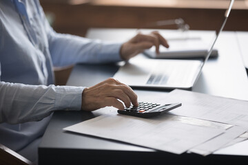 Unknown mature accountant sit at workplace desk working with lot of invoices, financial documents,...