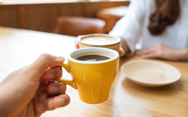 Closeup image of a young couple people clinking coffee cups together in cafe