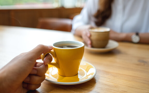 Closeup image of a young couple holding and drinking coffee together in cafe
