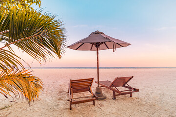 Fototapeta na wymiar Perfect tropical sunset scenery, two sun beds, loungers, umbrella under palm tree. White sand, sea view with horizon, colorful twilight sky, calmness and relaxation. Inspirational beach resort hotel